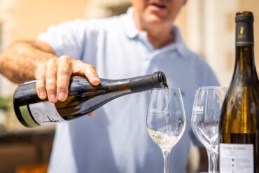 Adult pouring white wine into a glass outdoors at a wine tasting event.