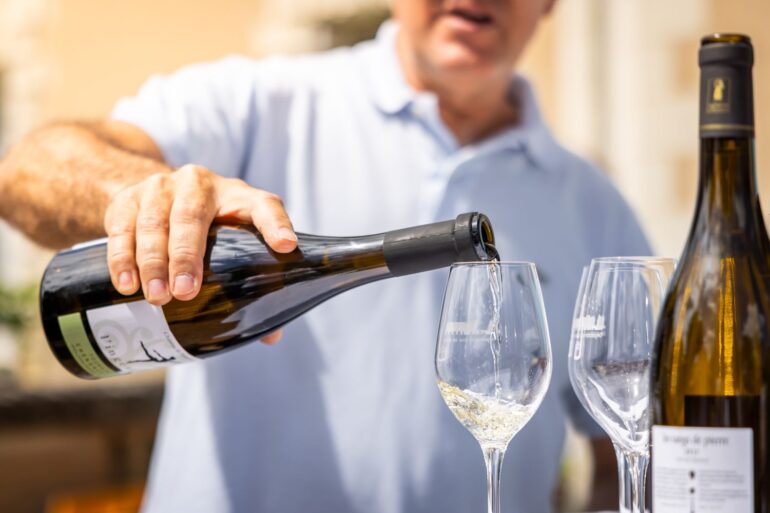 Adult pouring white wine into a glass outdoors at a wine tasting event.