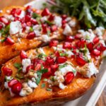 Baked sweet potatoes topped with feta cheese, pomegranate, herbs, and served with fresh greens.