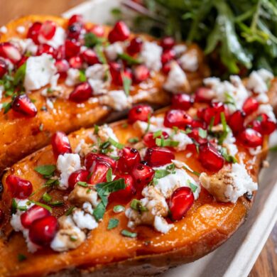 Baked sweet potatoes topped with feta cheese, pomegranate, herbs, and served with fresh greens.