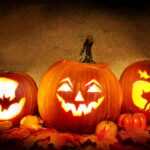 3 carved jack o lanterns lit up on a mantle ready for halloween night
