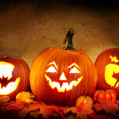 3 carved jack o lanterns lit up on a mantle ready for halloween night