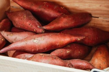 A store crate of fresh, uncooked sweet potatoes ready to be chosen