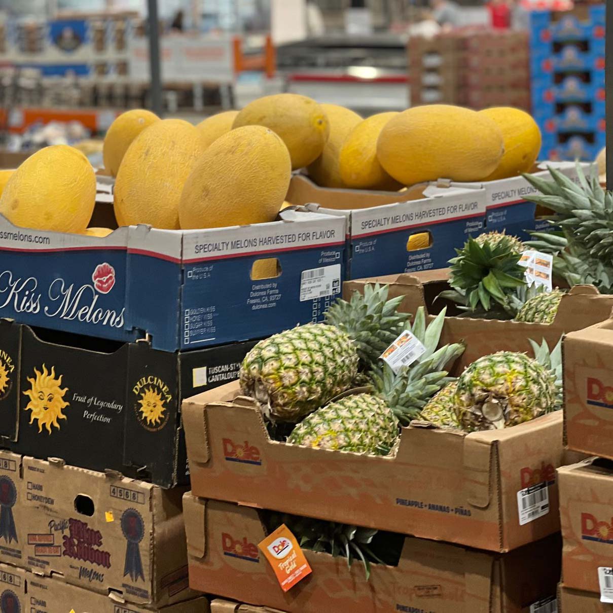 pineapples stacked in cardboard crates next to melons in a produce section of a food market