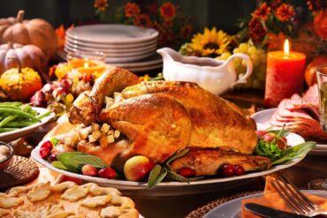 A delicious roasted turkey on a festive Thanksgiving table with all the fixings. Candles and flowers for ambiance.