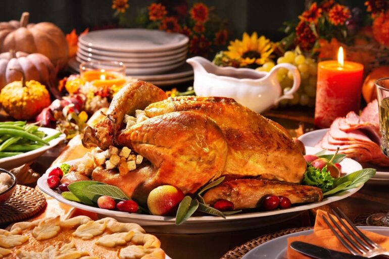 A delicious roasted turkey on a festive Thanksgiving table with all the fixings. Candles and flowers for ambiance.