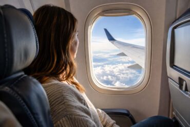 a woman on a commercial flight in the window set looking out at the wing above the clouds