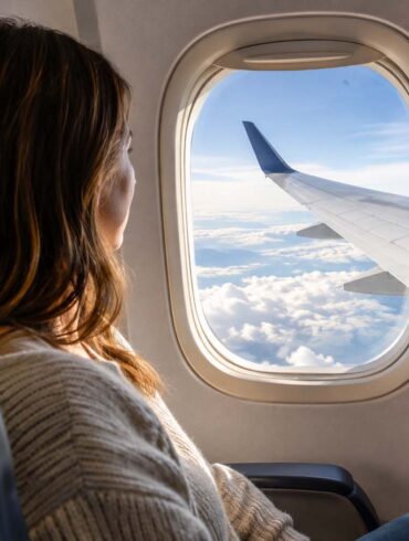 a woman on a commercial flight in the window set looking out at the wing above the clouds