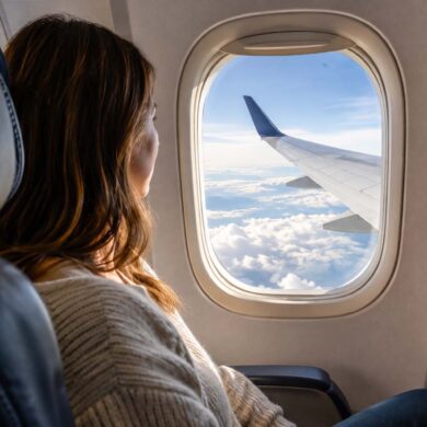 a woman on a commercial flight in the window set looking out at the wing above the clouds