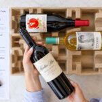 A woman opening a gift package of wine bottles with tasting note cards