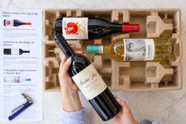 A woman opening a gift package of wine bottles with tasting note cards