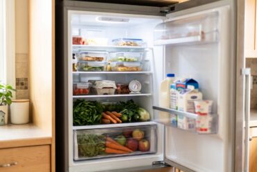 Open refrigerator with a thermometer, leftovers in shallow containers and produce stored unwashed