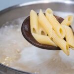 a bot of boiling pasta water with a spoonful of penne