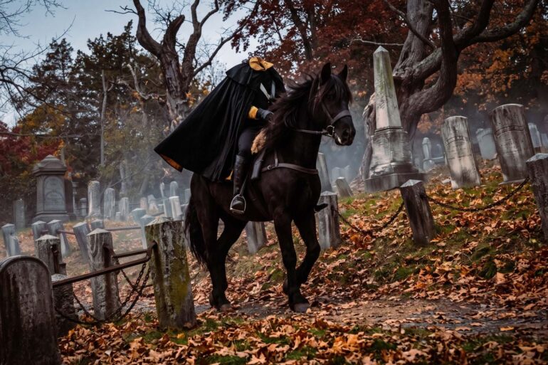 A realistic depiction of the Headless Horseman riding a black horse through a historic, autumn cemetery. He wears a dark cloak with a yellow-lined collar where his head should be. The path is covered in fallen orange and brown leaves, surrounded by old, weathered tombstones and bare trees under a moody, overcast sky.