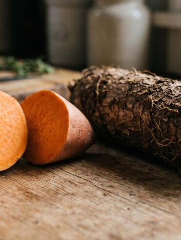 a close up side by side shot of a sweet potato and a yam on a rustic table