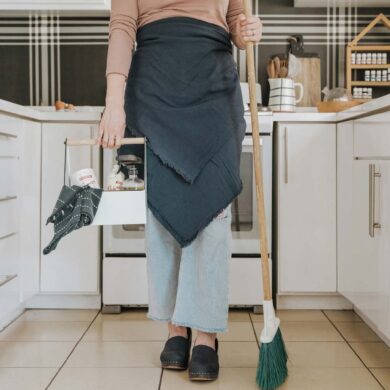 a woman standing in a kitchen holding a broom and cleaning supplies