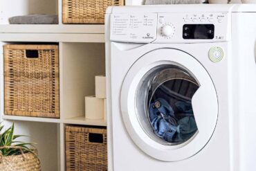 an up close shot of a washing machine in a laundry room with the door closed and wet clothes inside