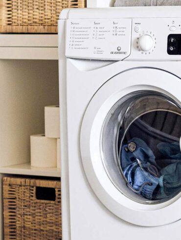 an up close shot of a washing machine in a laundry room with the door closed and wet clothes inside