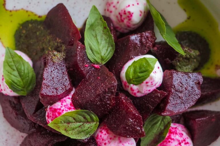 a close up of a fresh beet salad with basil leaves and cheese