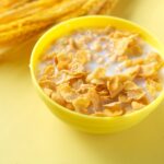 A bowl of corn flakes with milk on a table next to wheat husks