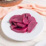 a plate of sliced pickled beets on a wooden table