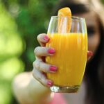 close up of a woman holding up a large glass or orange juice to the camera