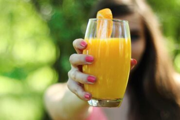 close up of a woman holding up a large glass or orange juice to the camera