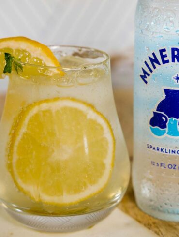 a bottle of sparkling water next a filled glass with lemon