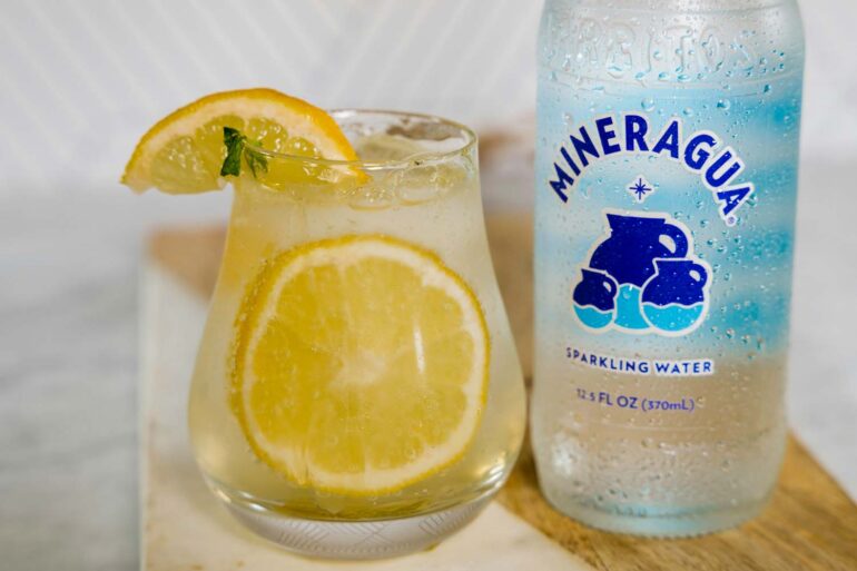 a bottle of sparkling water next a filled glass with lemon