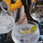 a bartender making gin and tonics while pouring tonic water into the cocktail