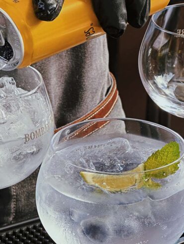 a bartender making gin and tonics while pouring tonic water into the cocktail