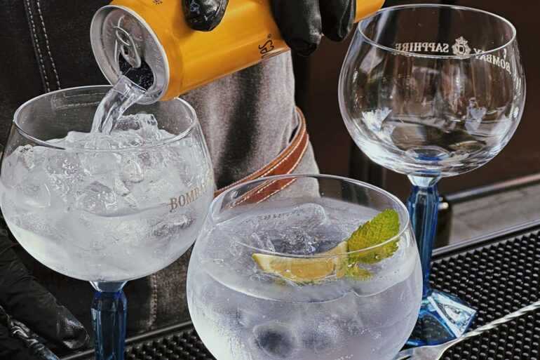 a bartender making gin and tonics while pouring tonic water into the cocktail