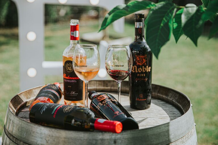 Rustic display of bottled wines and glasses on a wooden barrel in an outdoor setting.