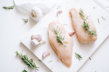 Top view of raw chicken breasts with rosemary and garlic