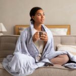 a woman drinking tea wrapped in a blanket on her sofa