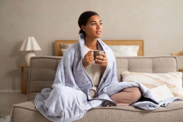 a woman drinking tea wrapped in a blanket on her sofa