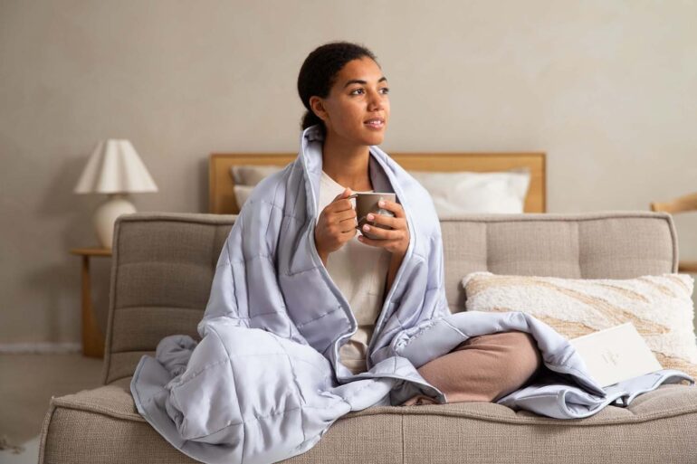 a woman drinking tea wrapped in a blanket on her sofa