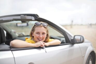 a woman in her 20's leaning out of a rental car convertible window holding keys