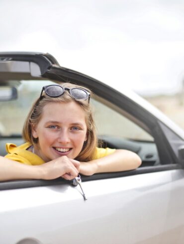 a woman in her 20's leaning out of a rental car convertible window holding keys