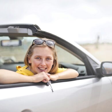 a woman in her 20's leaning out of a rental car convertible window holding keys